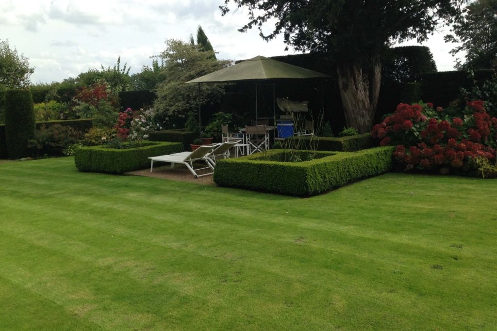 Pelouse tondue et haies de buis taillées autour d’un coin salon de jardin