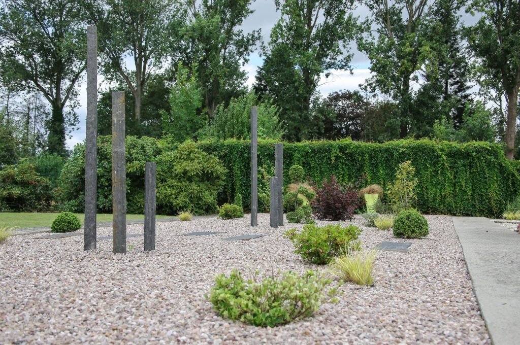 Jardin minéral aux stèles d’ardoise, graviers et massifs d’arbustes devant une haie